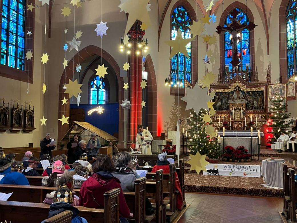 Das Bild zeigt eine große Gruppe von Sternsingern im Gottesdienst von Hinten Richtung Eingang auf den Altar fotografiert.