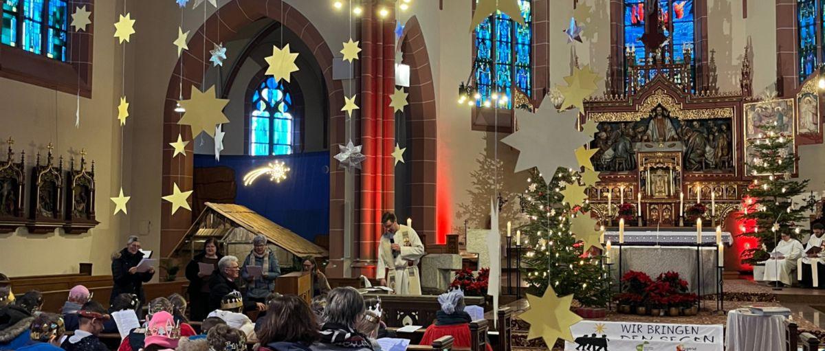 Das Bild zeigt eine große Gruppe von Sternsingern im Gottesdienst von Hinten Richtung Eingang auf den Altar fotografiert.
