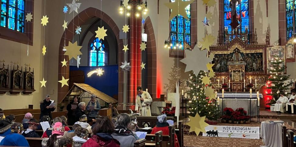 Das Bild zeigt eine große Gruppe von Sternsingern im Gottesdienst von Hinten Richtung Eingang auf den Altar fotografiert.