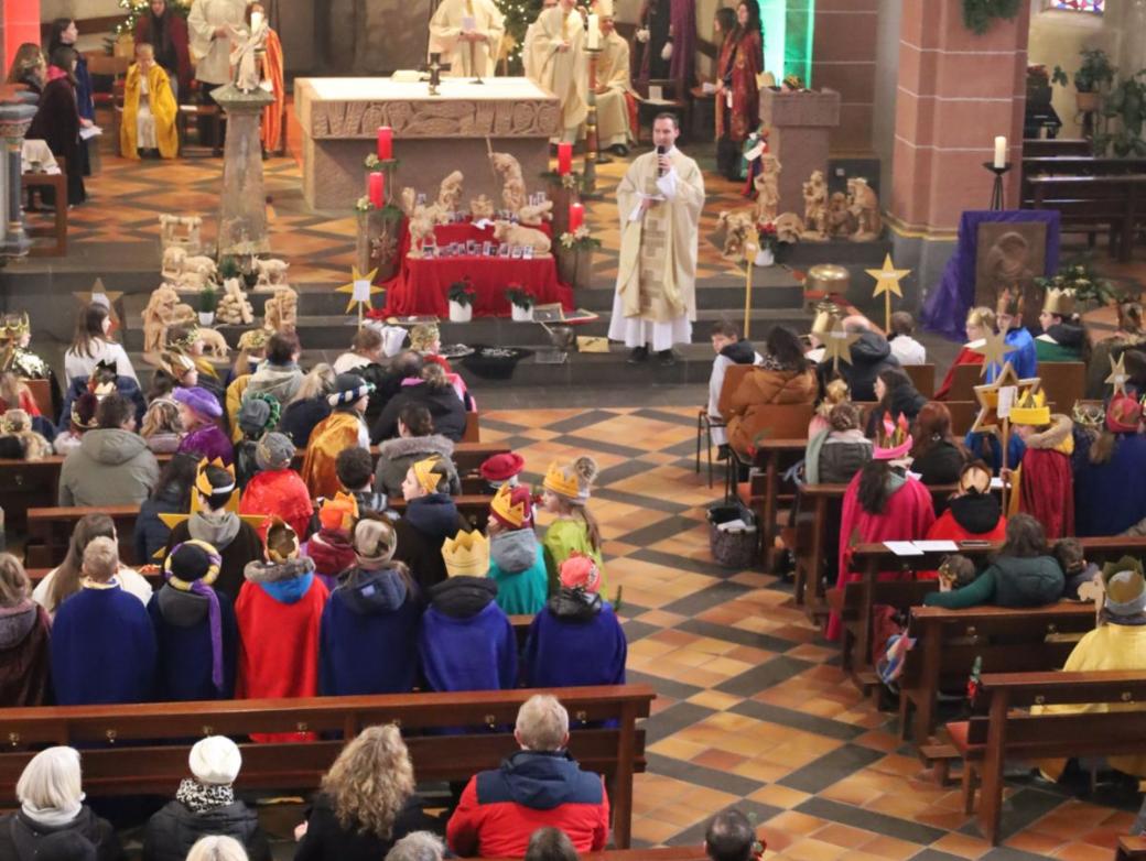 Das Bild zeigt eine große Gruppe von Sternsingern von oben/vom Eingang in Richtung Altar fotografiert.