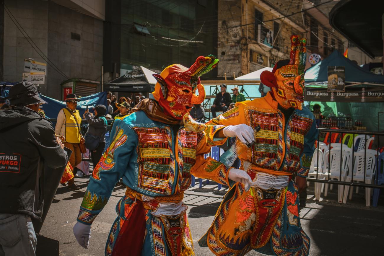 Auf dem Foto ist ein bunt maskierter und verkleideter Tänzer zu sehen. Er verkörpert den KUSILLO, eine mythologische und eine folkloristische Figur der bolivianischen Kultur, insbesondere der Andenregion.