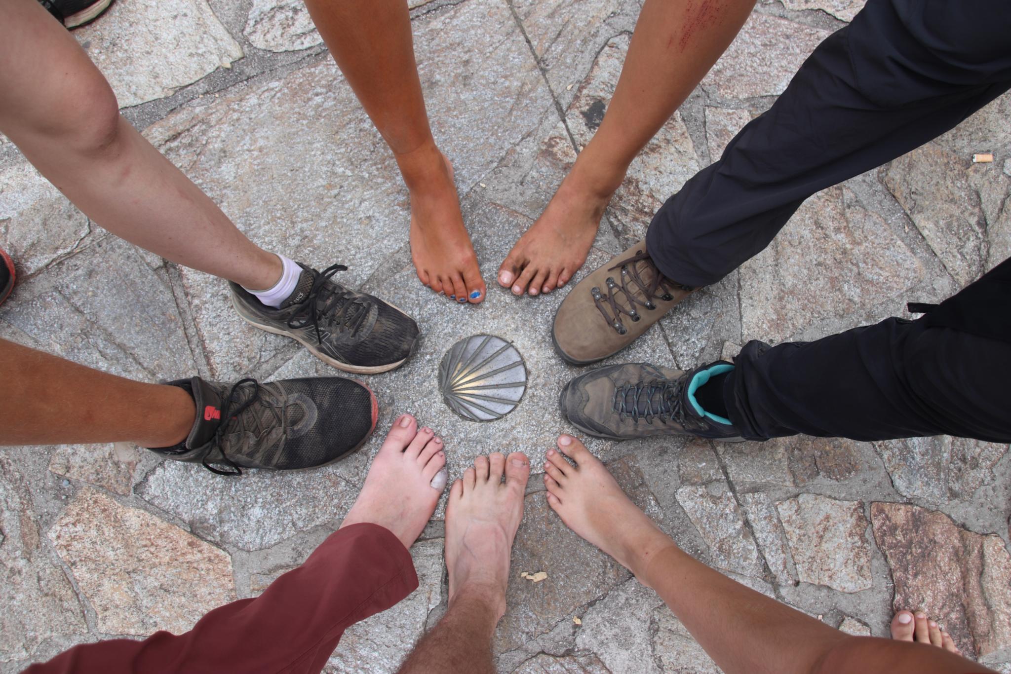 Junge Menschen stellen ihre Füße rund um das Symbol des Jakobsweges.