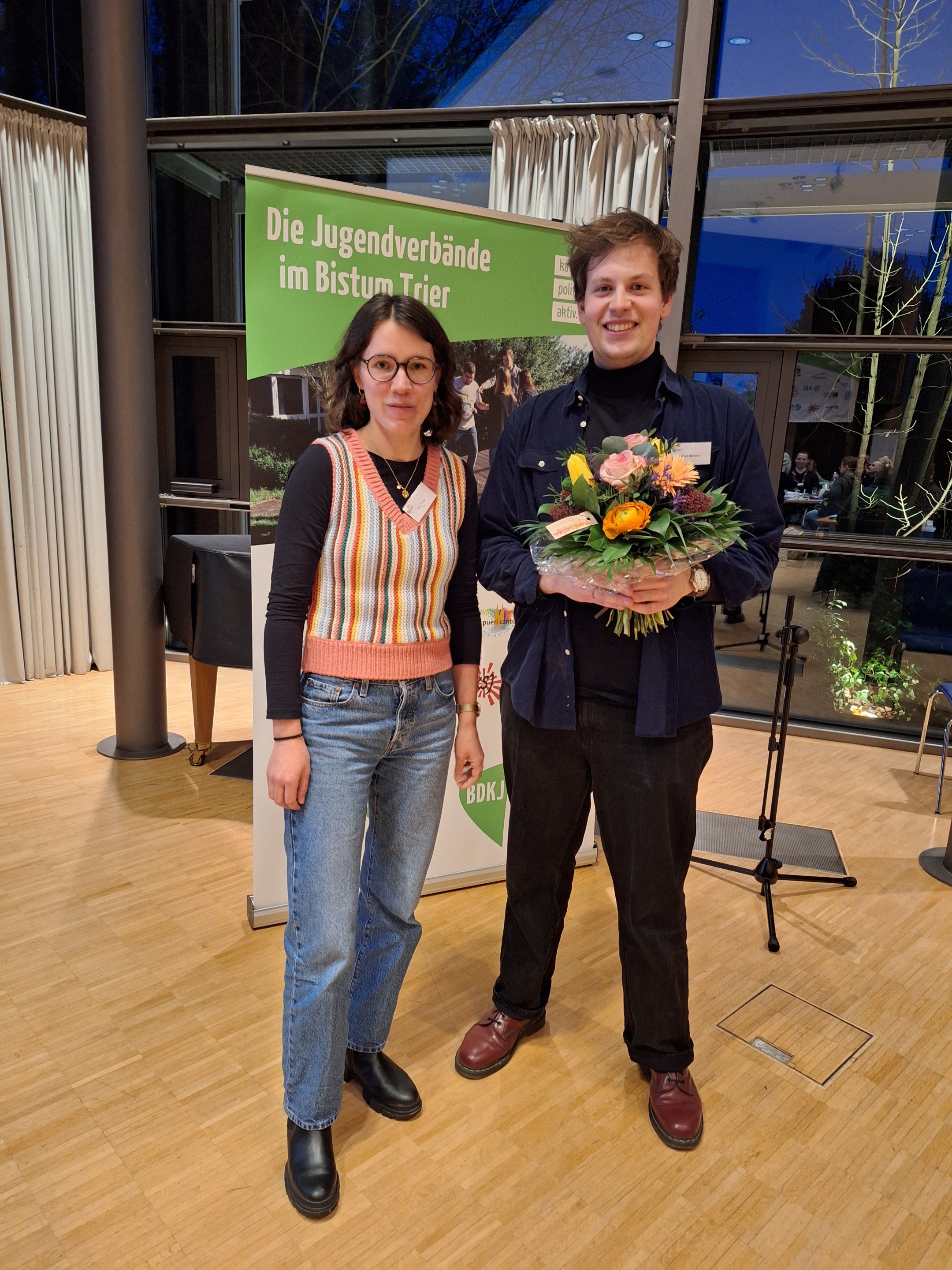 Das Bild zeigt zwei Personen. Eine hält einen Blumenstrauß