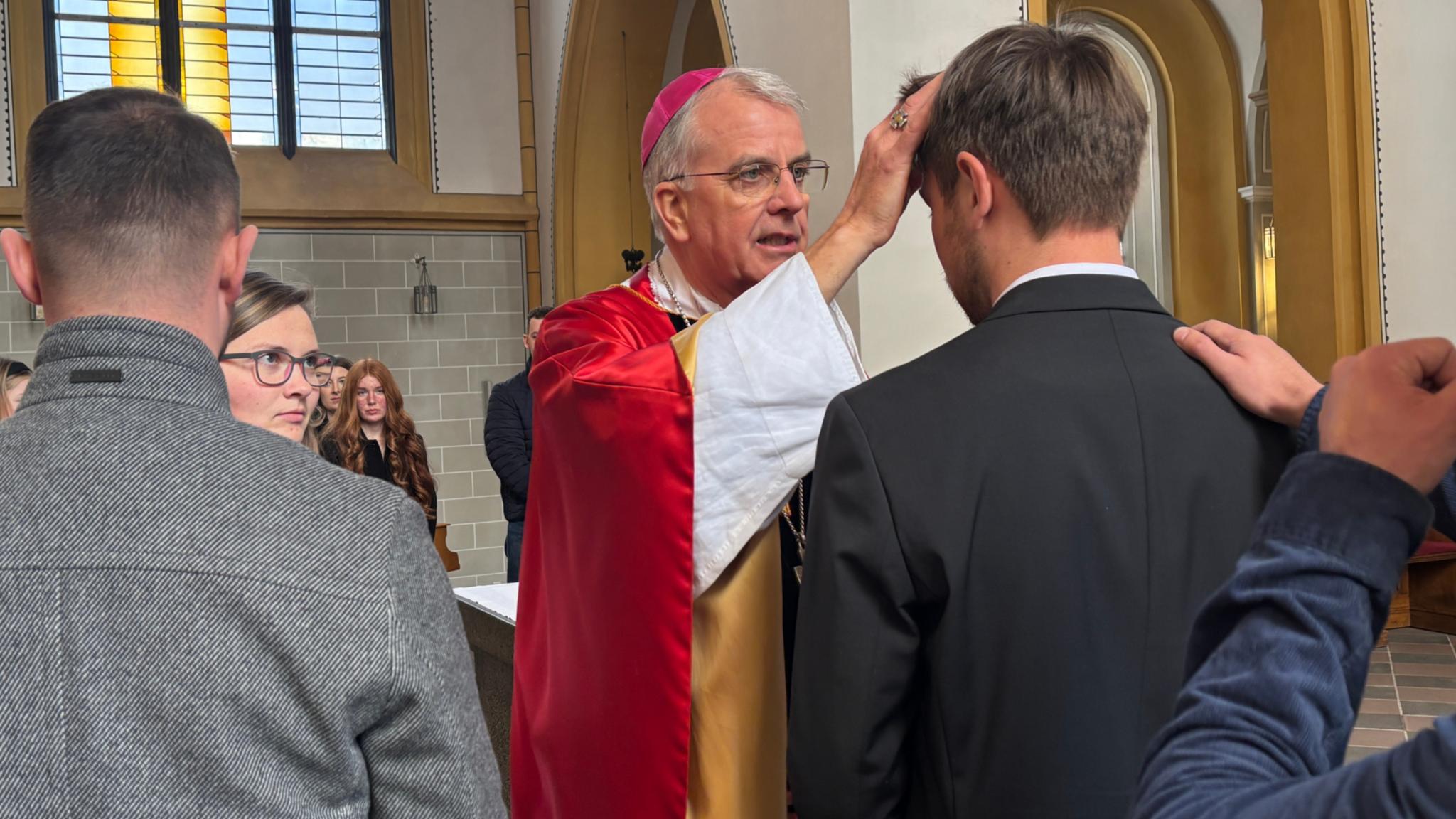 Weihbischof Peters macht einem jungen Erwachsenen das Kreuzzeichen auf die Stirn